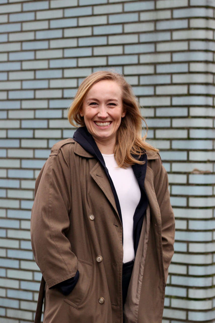 Blonde woman laughing in front of pale blue tiled wall