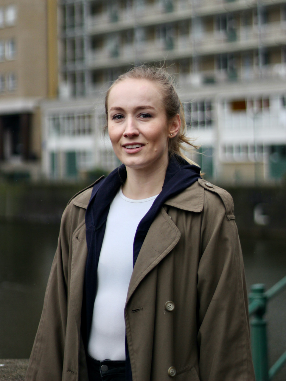 Blonde woman in brown coat in front of buildings