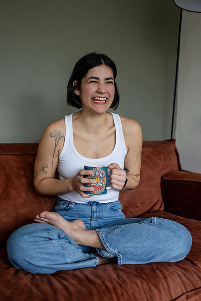 portretfotograaf blanke vrouw met zwart haar glimlachend op een bank met een mok thee portrait photographer in the Netherlands white woman with black hair smiling on a sofa holding a mug of tea