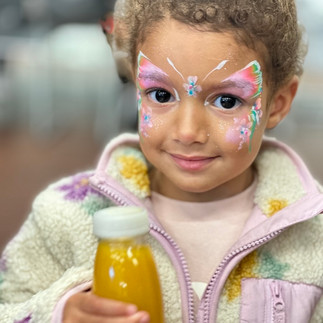 Little girl with her face painted like a butterfly holding her drink