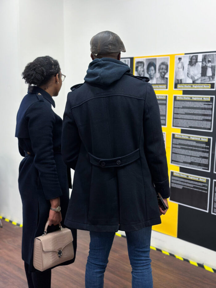 Woman and man curated stories from nurses on a wall in the Strength in Service Exhibition, the stories are on yellow and black columns
