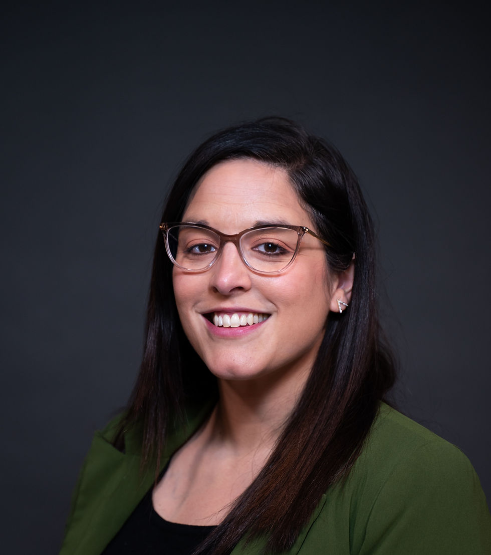 Woman with dark hair and glasses smiles at the camera with a dark grey background.