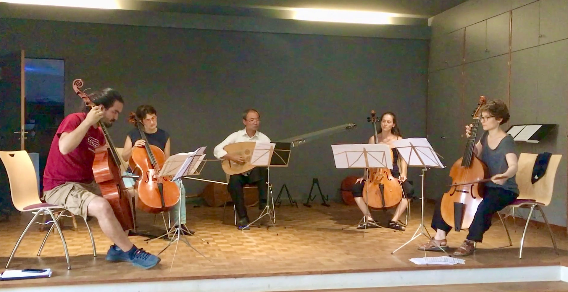 5 Musizierende proben: Gambe, Cello, Theorbe, Cello, Gambe. Alle außer Theorbe spielen linkshändig.