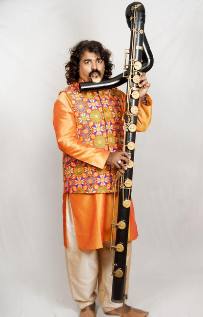 Pravin Godkhindi in a bright orange robe playing the contrabassflute right-handed