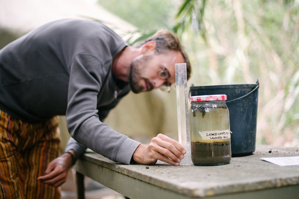 A person measuring soil layers in a jar using a rule