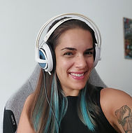 Smiling woman wearing white headphones, sitting in grey chair with tattoo.