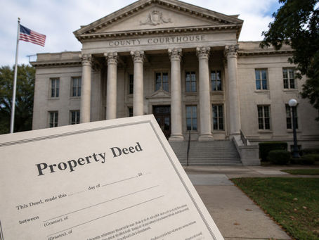 Close-up of a property deed in front of a classical courthouse with columns. A U.S. flag waves nearby. Bright, daytime setting.