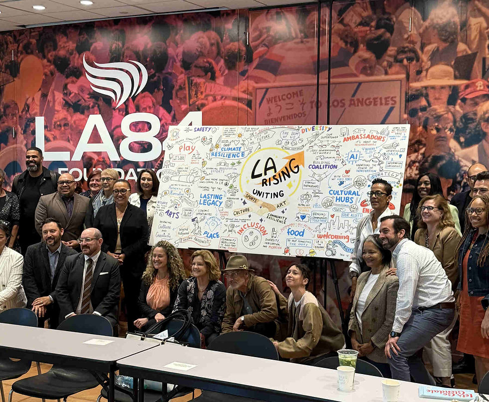 A group photo of attendees posing in front of a large illustrated board at an LA84 Foundation event