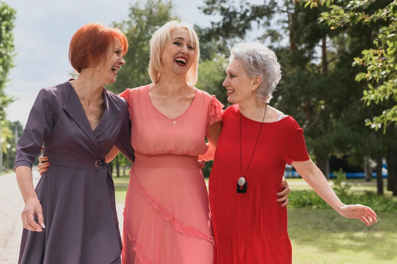 Four middle-aged women walking side by side outdoors, laughing together and appearing relaxed and co