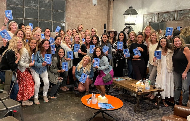 Several women gather in a coffee shop holding copies of the book Second Half by Kelsey Chittick