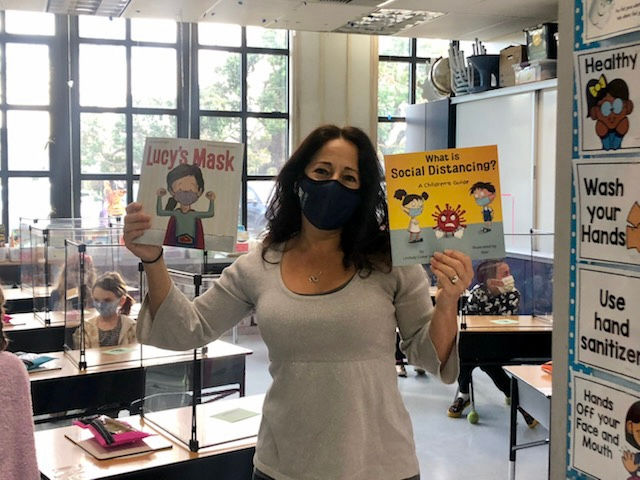 Teacher Alisa Lister stands in her classroom holding two picture books about the coronavirus pandemic.