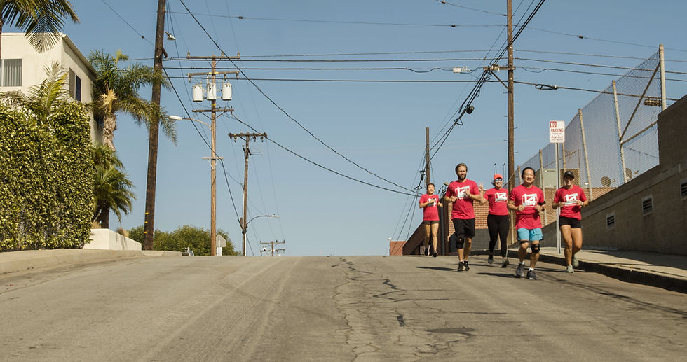 Five runners in matching red "Gate 14" shirts smile while running down a street
