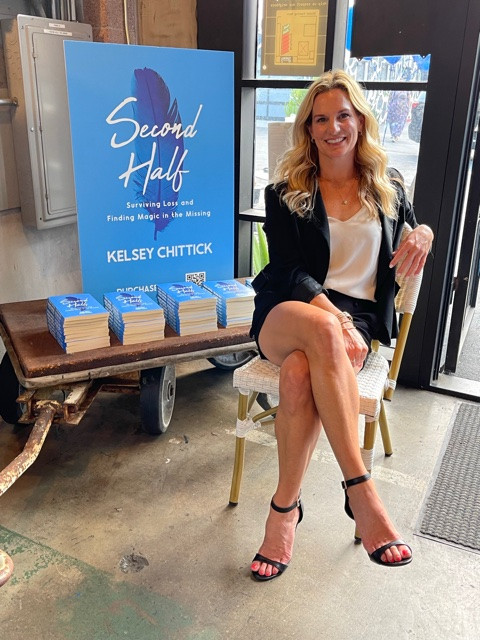 Author Kelsey Chittick poses alongside stacks of her memoir