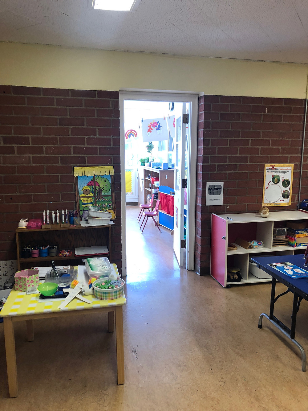 The tidy main playroom of El Segundo Co-op Nursery School is silhouetted against an door opening into a brightly lit classroom