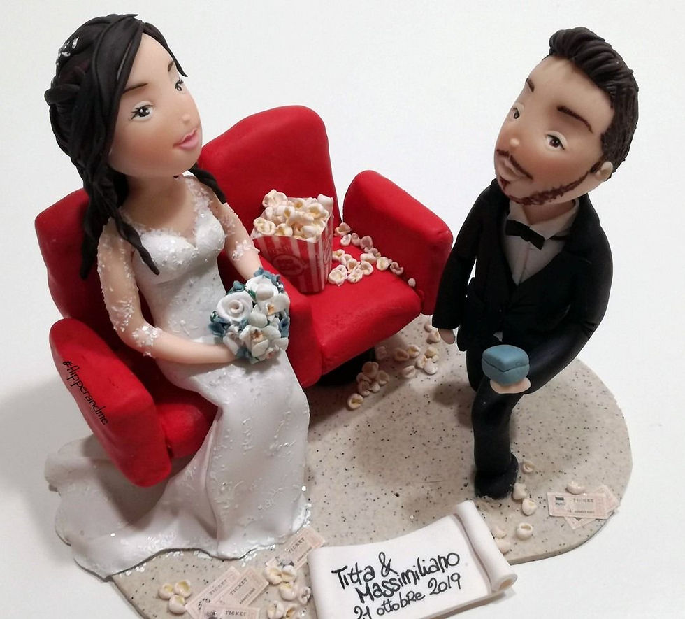 Cake topper matrimonio personalizzato con sposa seduta su una poltrona rossa, sposo in piedi e popcorn, ispirato a una proposta di matrimonio al cinema.