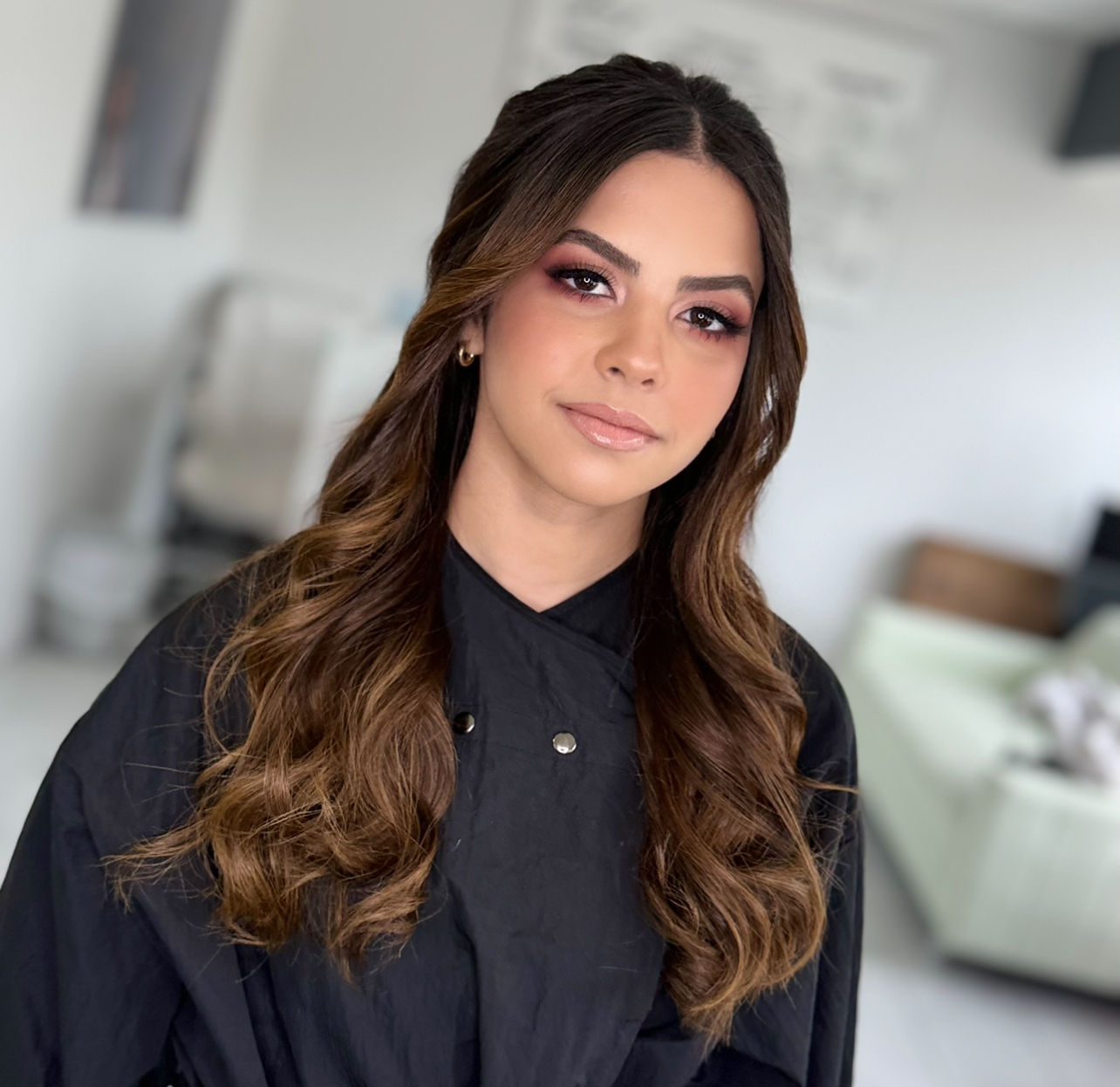 Young woman with long wavy brown hair wearing a black shirt Natural Glam.