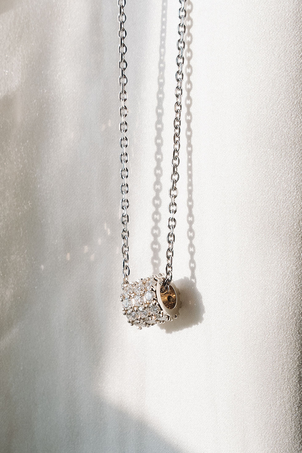 Pavé pendant necklace hanging in front of white fabric.