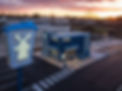 Aerial photo of a Dutch Bros Coffee drive-thru building with branded signage, outdoor seating, and an adjacent parking lot at sunset.