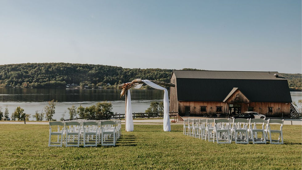 White chairs set up for an outdoor ceremony on the lawn at Bates Barn, with Belleisle Bay