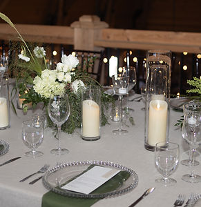 A reception table set with candles, glassware and greenery