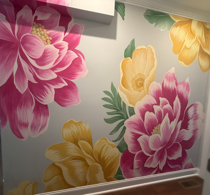 Hand-painted floral wall mural with large pink and yellow flowers on a light gray accent wall in a modern residential hallway.