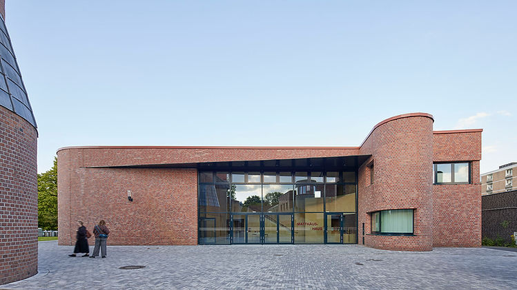 Blick über einen grau gepflasterten Platz auf den gesamten Eingangsbereich des neuen Gemeindezentrum St. Matthäus