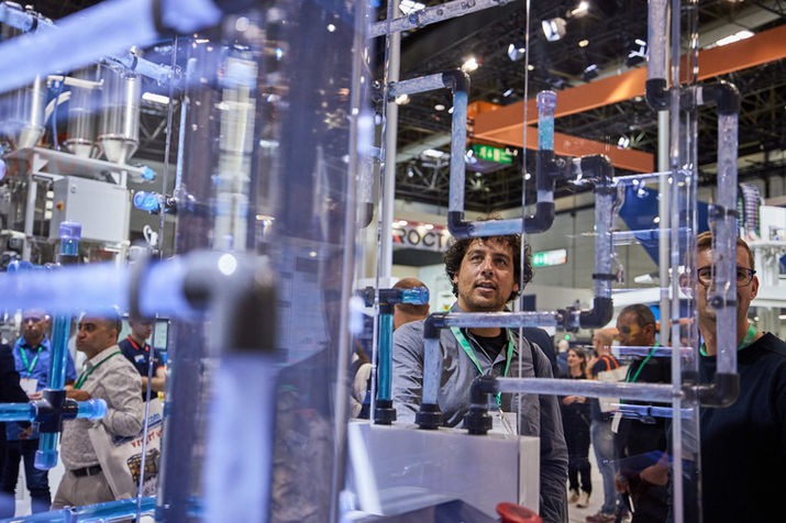 Gelockter dunkelhaariger Mann hinter einem mit durchsichtigen Plastikröhren bestückten Schaukasten