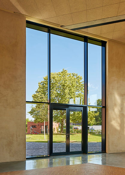 Blick aus einem Innenraum mit sehr großem Fenster auf einen grünen Baum auf einer Wiese vor dem neuen Gemeindezentrum St. Matthäus
