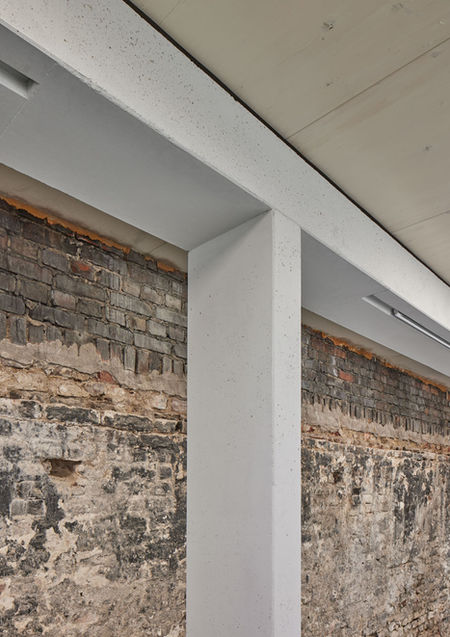 Detail eines neuen weissen Tragwerks bestehend aus einem t-förmigen Träger. Dahinter im Kontrast eine Wand aus alten Klinkern und anderen Steinen.