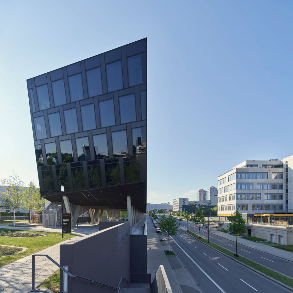 Die asymmetrische Fassade des Funke Medien Hauses bestehend aus flächig eingebauten Fenstern und dunklen Aluminium Fassadenteilen, auf der rechten Seite eine breite leere Strasse.
