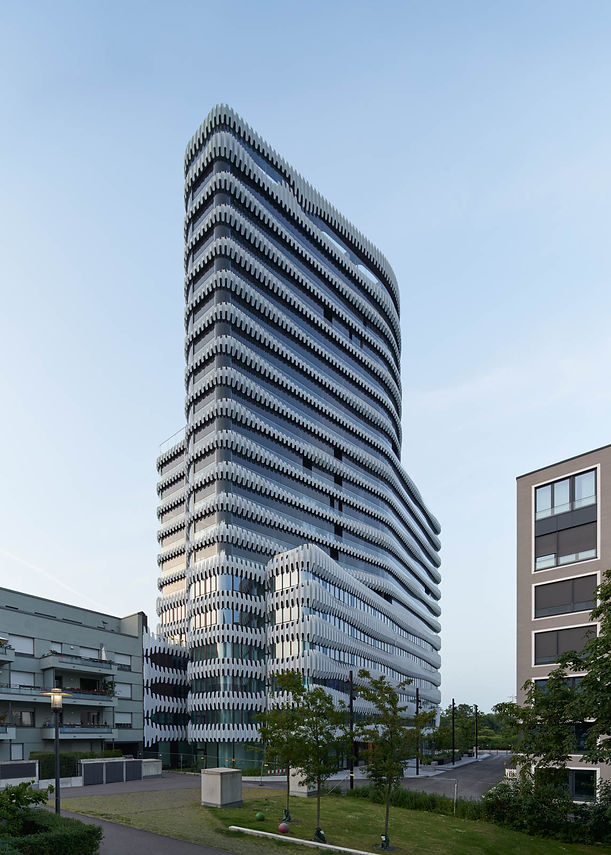 Die Süd-Westseite der drei weissen Türme des RKM 740 im Gegenlicht, im Vordergrund Wohnhäuser und ein begrünter Innenhof