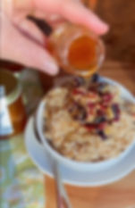 A bowl of hearty oatmeal is topped with nuts and berries as a person drizzles golden Sparkle & Honey, creating a wholesome and delicious breakfast.