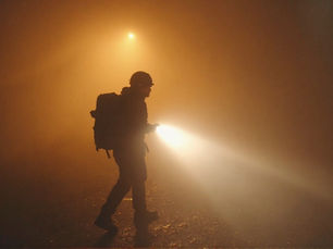 Silhouette of a person wearing a helmet, holding a flashlight in a foggy, orange-lit setting. The mood is mysterious and tense. Mars. Icarus scifi book.