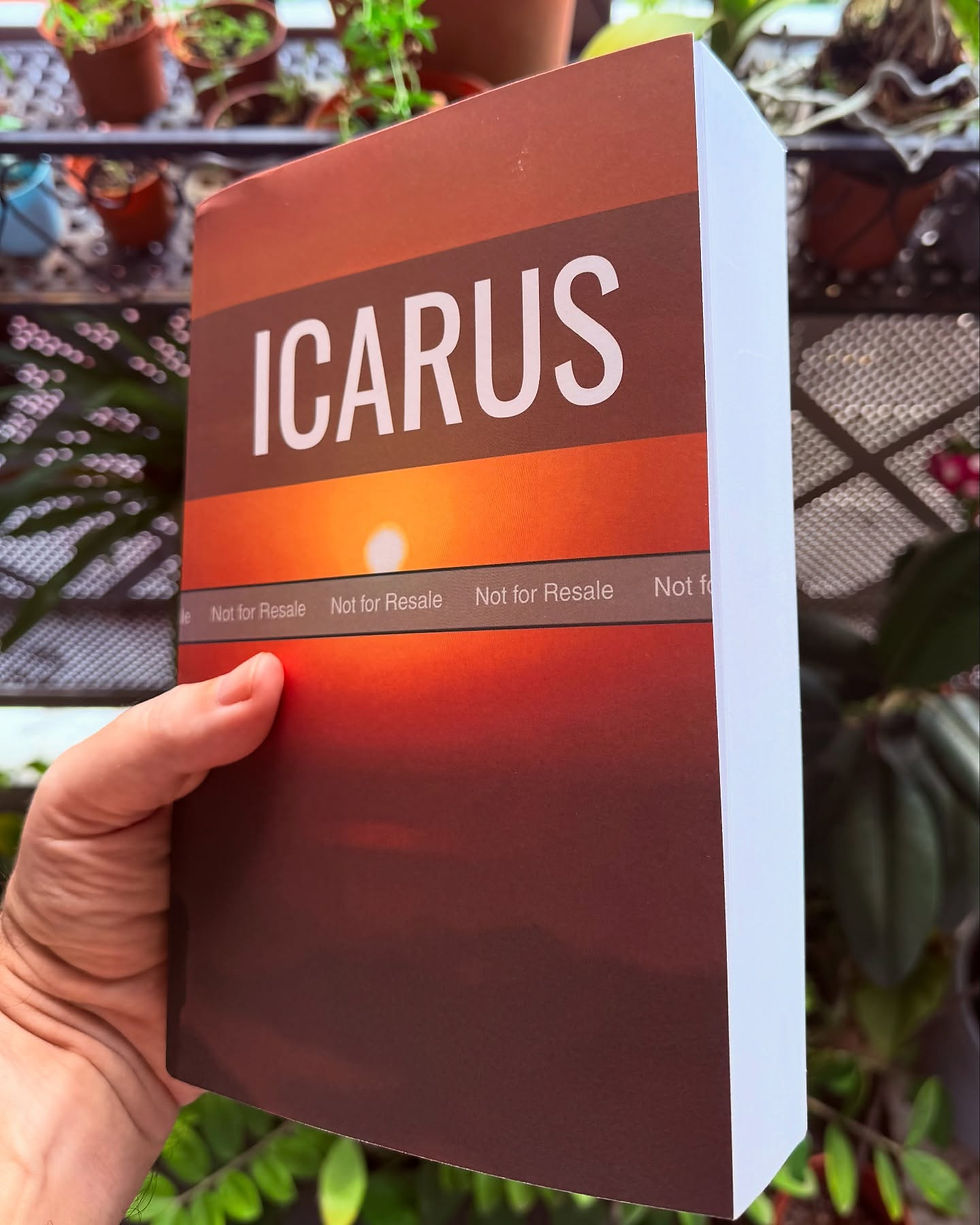 Hand holding a book titled "ICARUS" with an orange sunset cover. "Not for Resale" is printed below. Potted plants in the blurred background.
