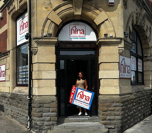 Nina standing with FOR SALE sign for Nina Estate Agents