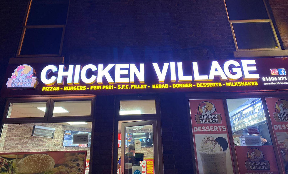 Illuminated sign for "Chicken Village" at night, advertising pizzas, burgers, kebabs, and more