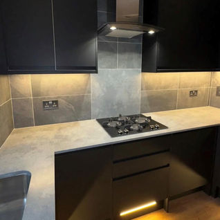 Black cabinets and cupboards, white worktops and LED warm lights installed underneath cabinets