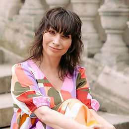 Paula Jones nutritional therapist profile photo smiling in a colourful patterned dress seated outdoors against a stone background