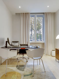 aménagement cabinet médical, bureau de consultation design, décoration cabinet libéral, mobilier de bureau moderne, chaises design blanches, lampe Pipistrello, buffet en bois suspendu, tapis graphique contemporain, décoration espace professionnel, rideaux beiges élégants, éclairage cabinet de soin, agencement bureau d'architecte, style minimaliste chic, cadre abstrait coloré, bibliothèque murale métal, espace de travail lumineux, parquet clair, architecture d'intérieur tertiaire, décoration bureau haut de gamme, mobilier professionnel contemporain.