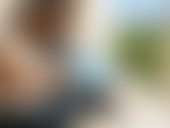 Pareja joven embarazada planeando la maternidad internacional, mirando un mapa del mundo en una tablet. En la mesa hay escarpines de bebé, un pasaporte y documentos de GNP Seguros.