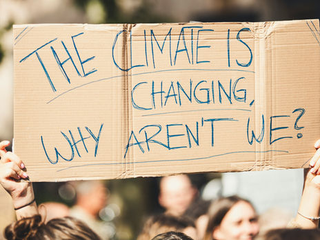 Person hält bei einer Demonstration ein Kartonschild mit der Aufschrift „The climate is changing, why aren’t we?“ hoch. Symbolisches Bild für Klimaschutz, Nachhaltigkeit und gesellschaftliche Verantwortung.