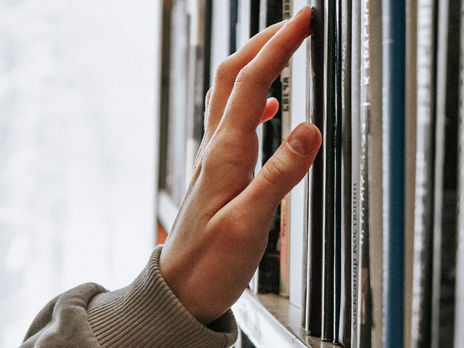 Hand greift nach einem Buch in einem Bücherregal als Symbol für Wissenszugang, Lernen und lebenslanges Lernen in der modernen Bildungswelt.