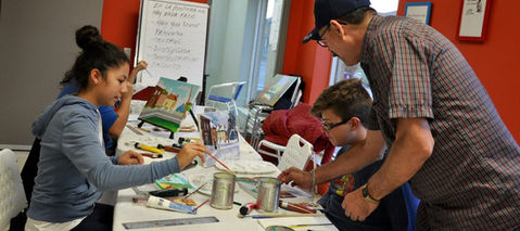 Adult man helps children as they participate in a painting event.