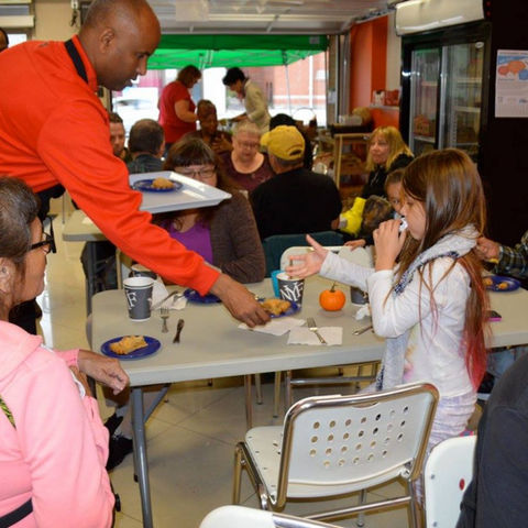 Man bends over and serves food to young girl.
