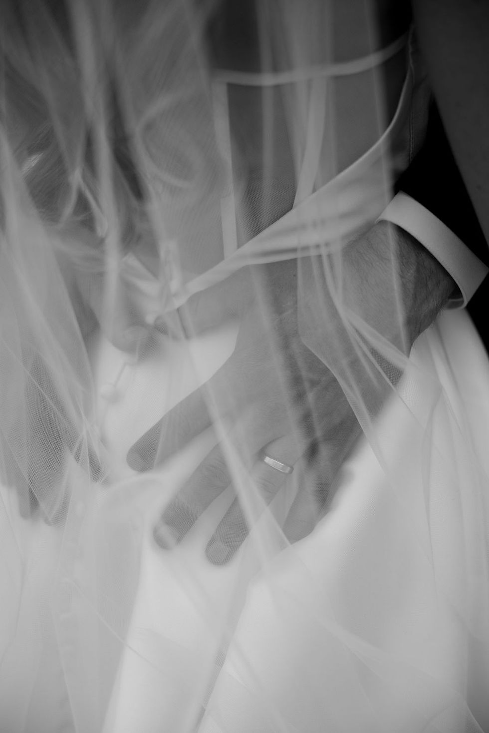 Black and white photo of close up of grooms ring hand on brides waist