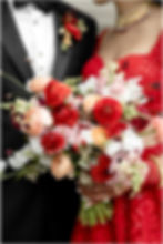 Bride in a red lehenga and groom in a black tuxedo close up detail photo of wedding flowers