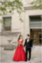 Bride in a red lehenga and groom in a black tuxedo walking hand in hand on the steps outside the Indianapolis Central Library