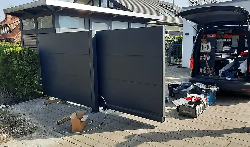 Das Nordzaun-Team bei der Montage einer Schiebtoranlage; im Hintergrund das Montagefahrzeug mit Arbeitsmaterialien auf der vorbereiteten Baustelle.