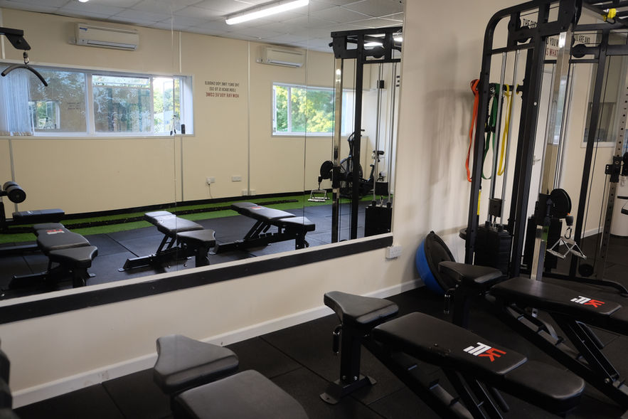 Three gym benches in front of a large mirror, cable machine to the right.