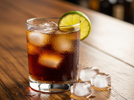 Ein Bourbon-Cola-Cocktail in einem Glas mit Eis und Limette, auf einer rustikalen Holztheke.